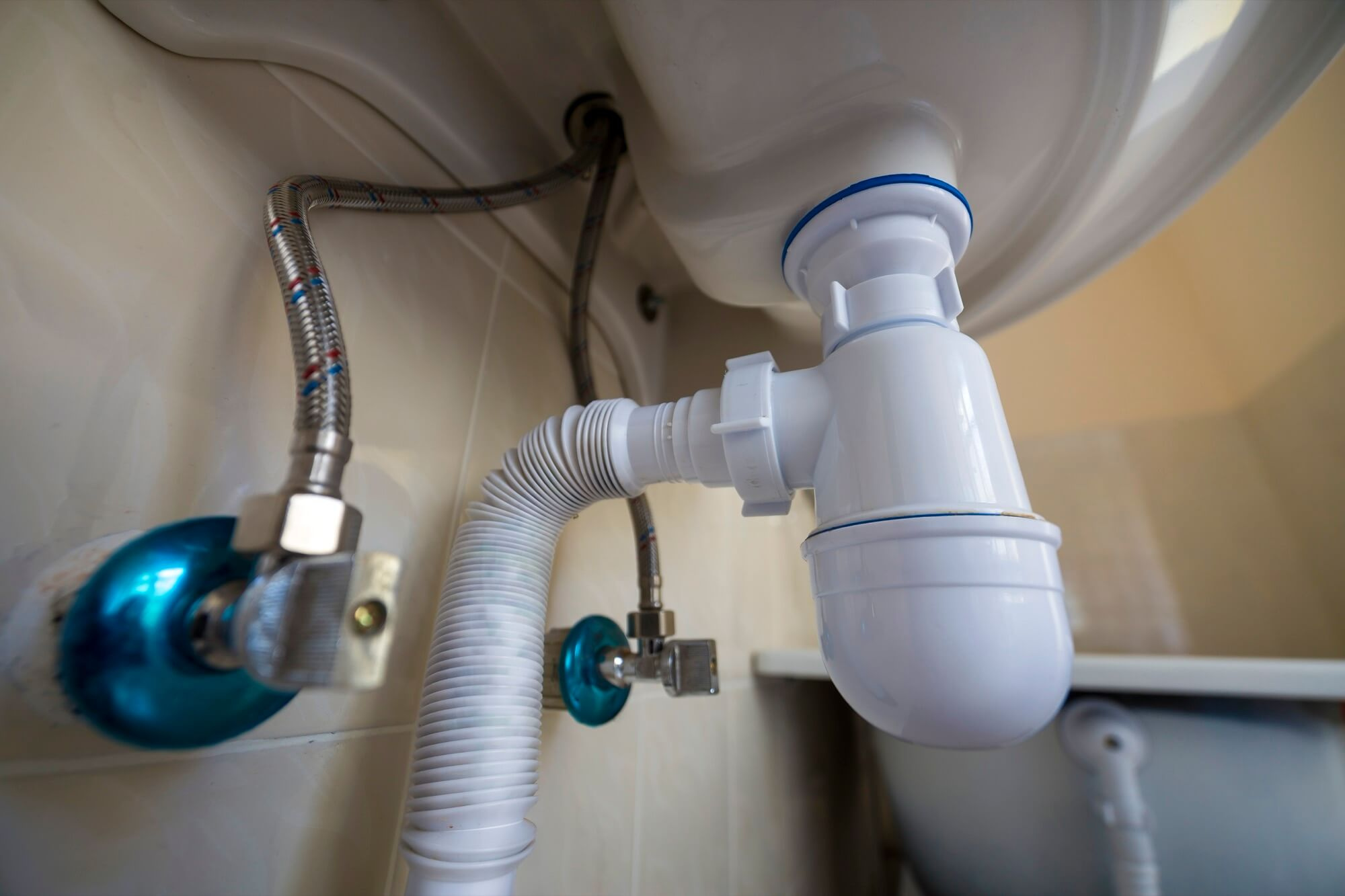 VVS-rör och ett vitt vattenlås i plast installerat under ett handfat i ett badrum.