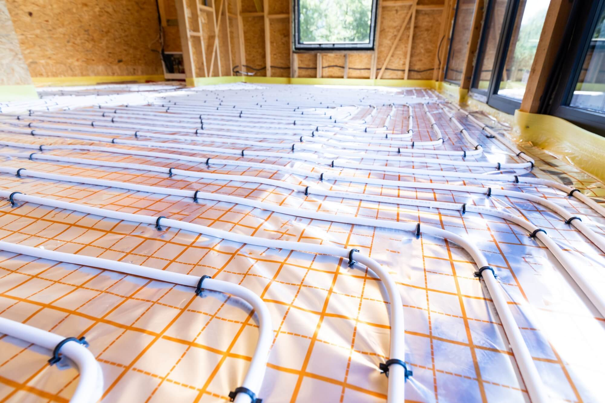 Installation av VVS för golvvärme i ett hus under uppbyggnad med trästomme.