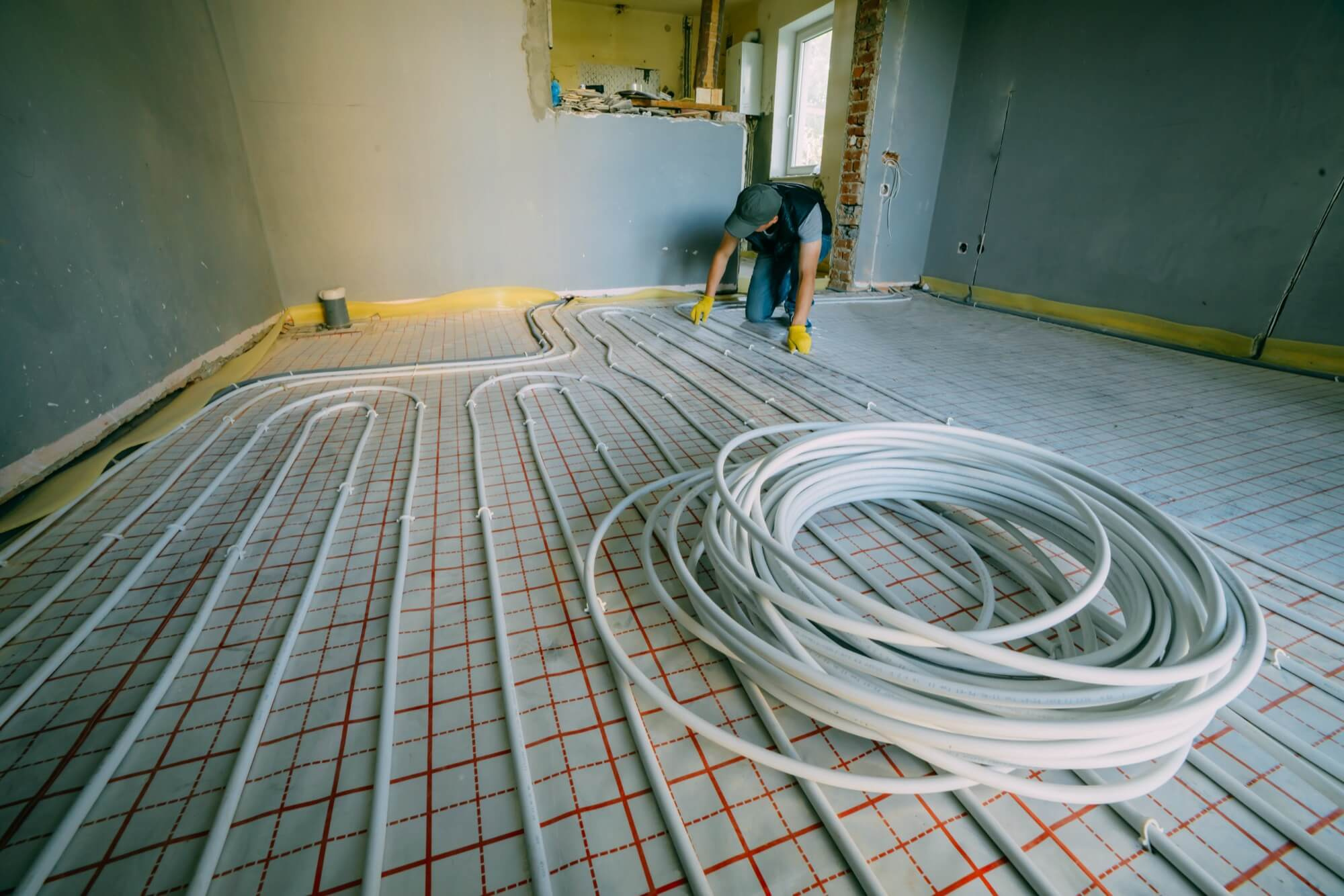 En VVS-montör som installerar rör för golvvärme, med en stor rulle rör i förgrunden.